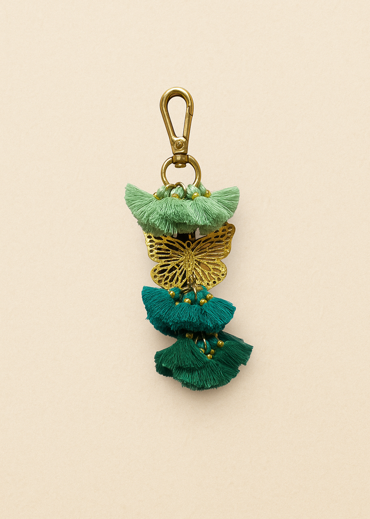 Decorative keychain with green and gold tassels on a beige background