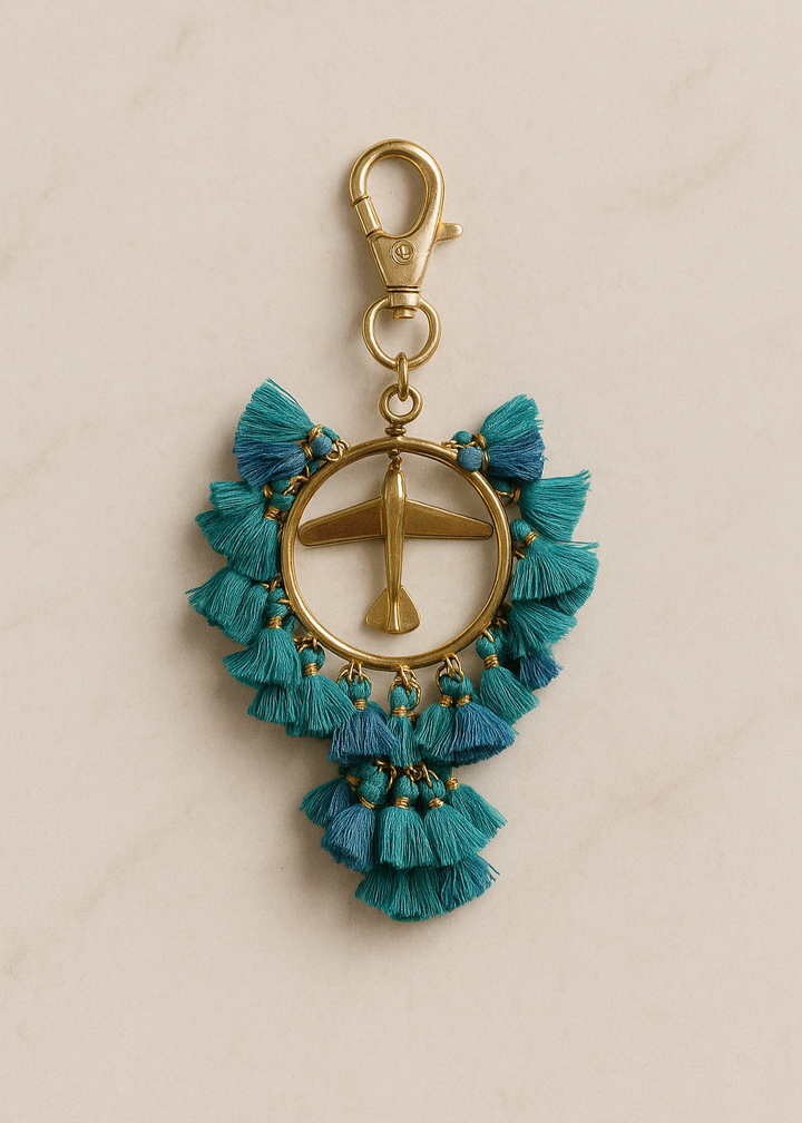 Keychain with blue tassels and gold airplane charm on a beige background