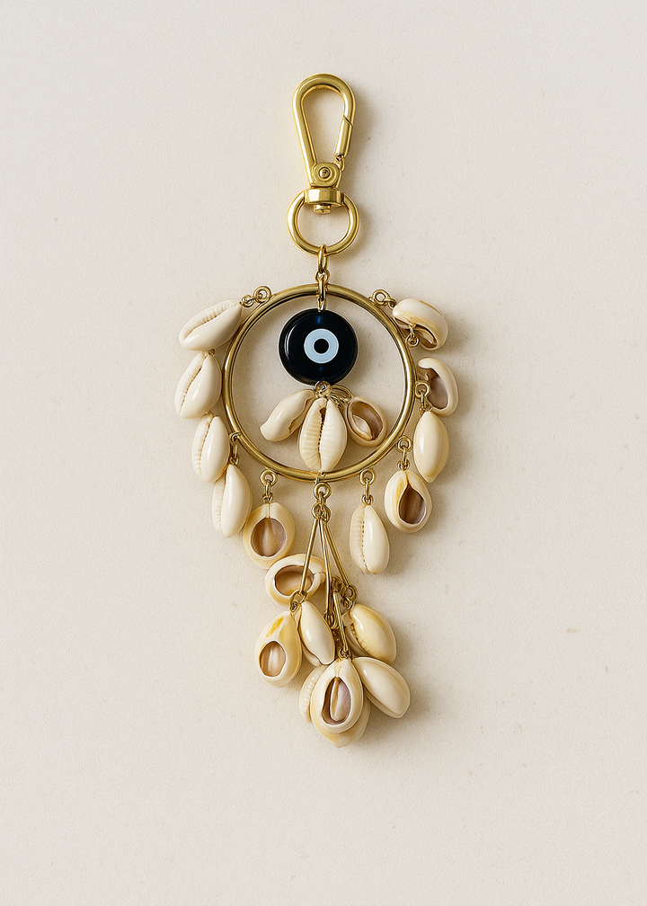 Decorative keychain with shell elements and a black evil eye charm on a beige background