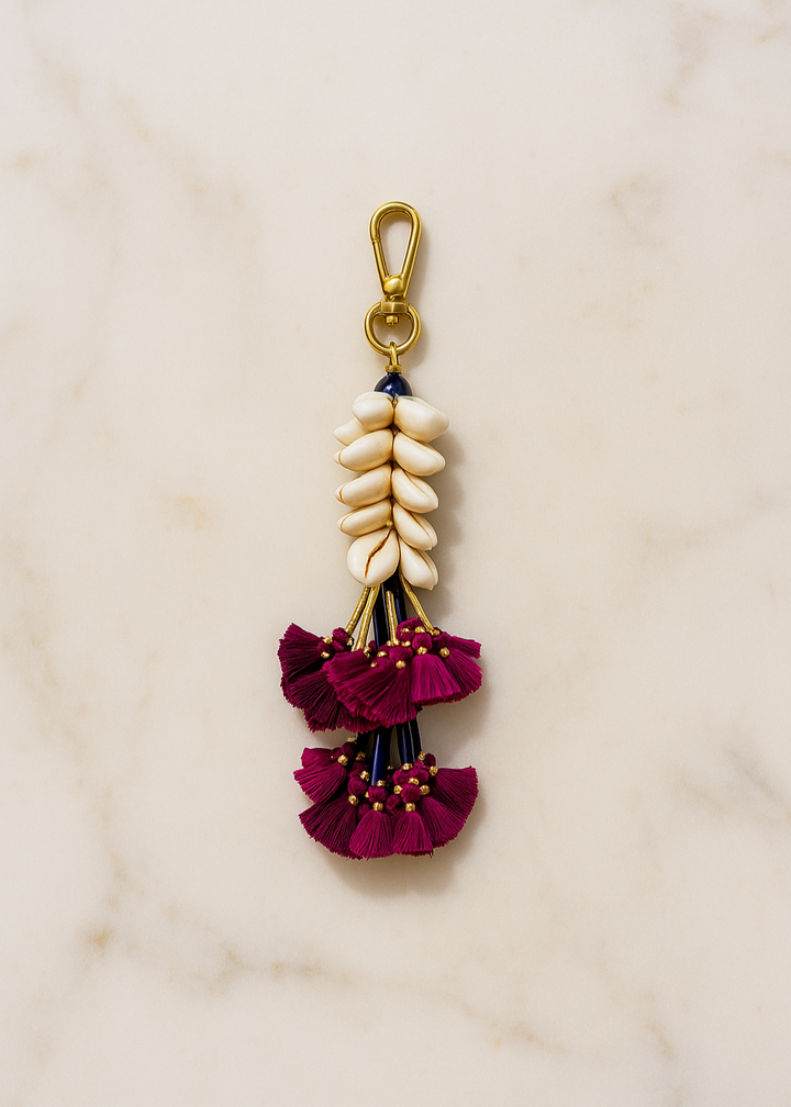 Decorative keychain with maroon floral elements and gold accents on a beige background