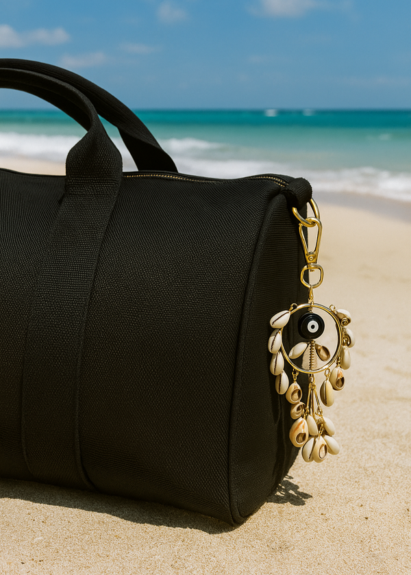 Black duffel bag with a decorative keychain on a sandy beach with ocean view