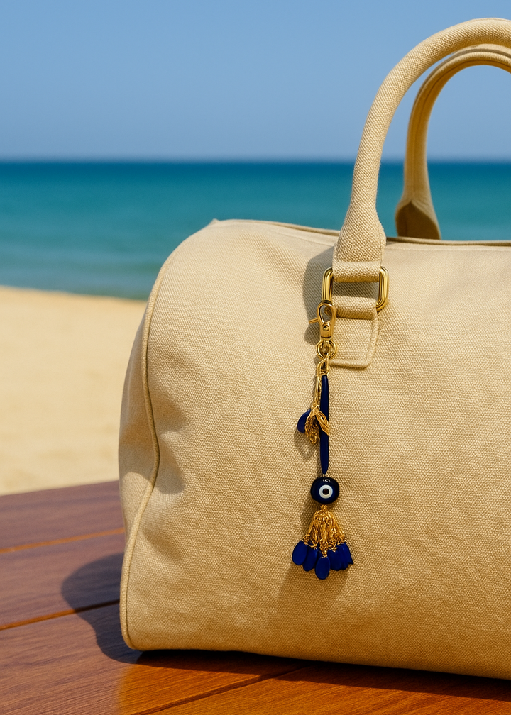 Beige handbag with a decorative keychain on a wooden surface with a blue sky and ocean background