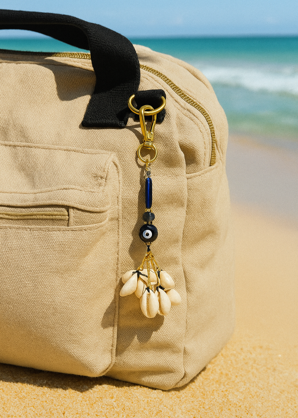 Beige bag with a keychain on a sandy beach with ocean in the background