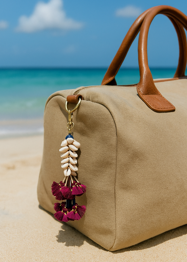 Beige handbag with a decorative keychain on a sandy beach with ocean view
