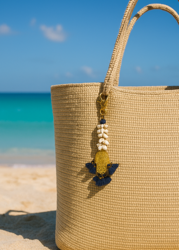 Beige straw bag with decorative charm on a sandy beach with ocean view