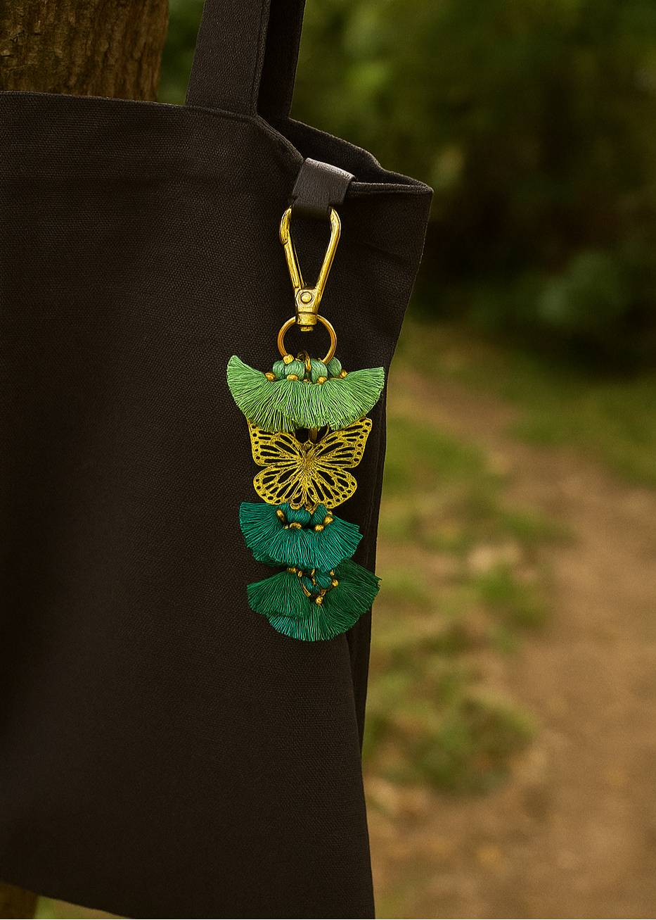 Black bag with a decorative green and gold butterfly pendant hanging from it, against a blurred natural background.