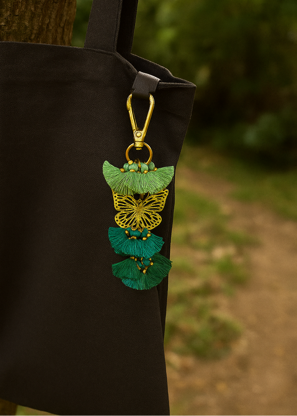 Black bag with a decorative green and gold butterfly pendant hanging from it, against a blurred natural background.