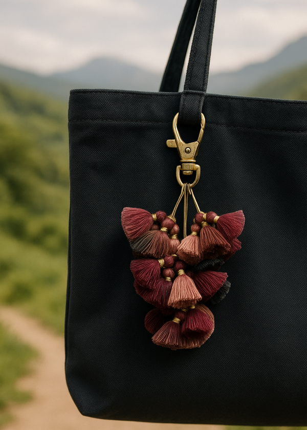 Black bag with a decorative keychain featuring tassels and beads against a blurred natural background