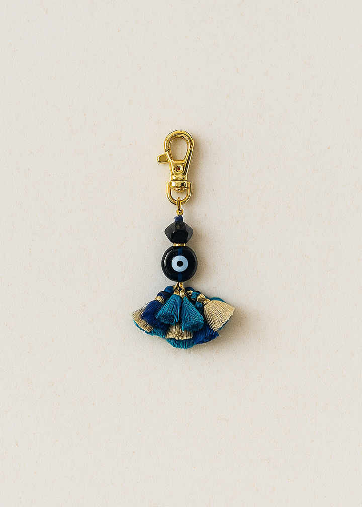 Decorative keychain with blue tassels and black bead on a beige background