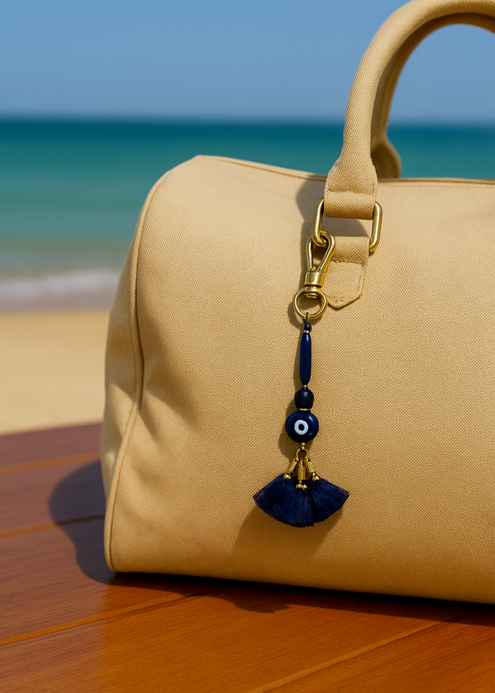Beige handbag with a blue evil eye charm on a wooden surface with a beach in the background